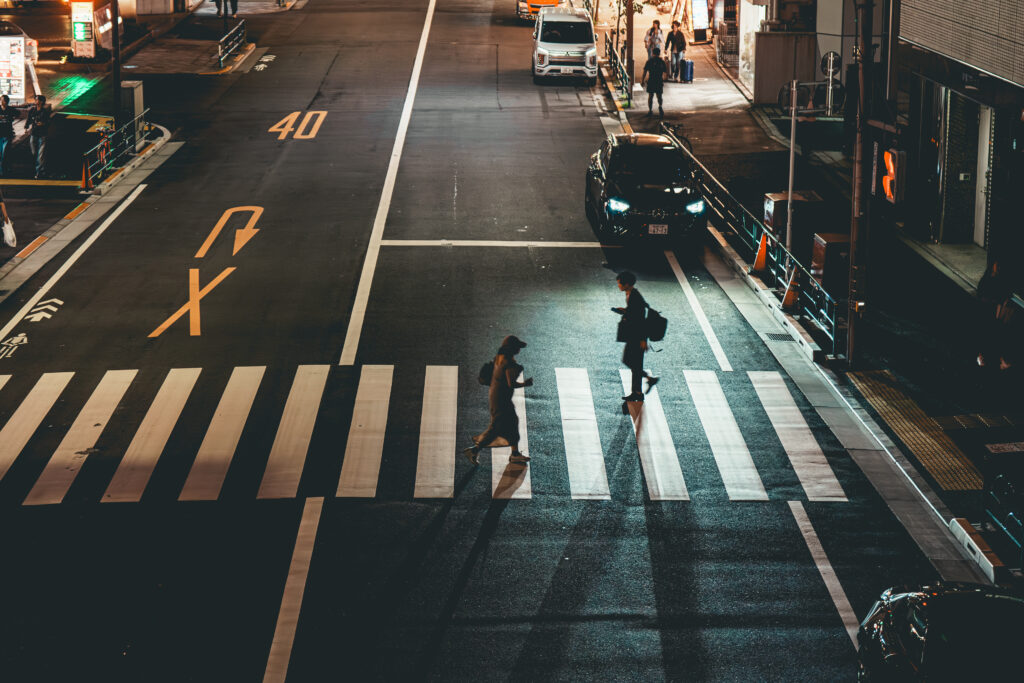 横断歩道を渡る人を照らす車のヘッドライト